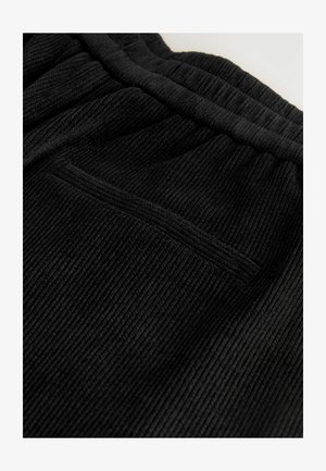Pantalons en tissu noir à rayures, présentant une surface texturée et une taille élastique. Comprend un petit détail de poche latérale discrète.
