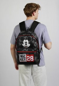 Mochila negra con diseño de Mickey Mouse, acentos rojos y texto blanco "MIC KEY 28"; presenta un patrón texturizado y correas para los hombros ajustables.