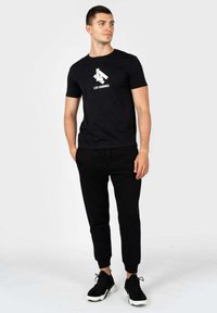Sort bomuld t-shirt med hvid "LES HOMMES" logo, parret med sorte sweatpants og sorte træningssko med hvide såler.