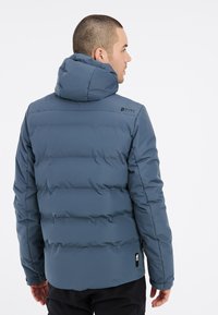 Blaue Daunenjacke mit Kapuze, gestepptem Design und elastischen Bündchen. Logo auf der oberen Rückseite platziert. Material wirkt glatt und strapazierfähig.