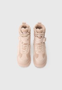 Botas altas color beige con cuello de piel texturizada, cierre frontal de cordones y una correa de velcro; fabricadas con materiales mixtos y suela gruesa de goma.