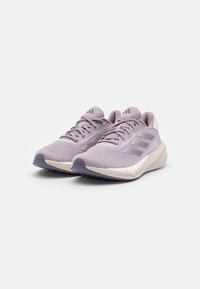 Zapatillas de running de color lavanda claro con parte superior de malla, tejido texturizado y tres franjas diagonales. Cuentan con una suela acolchada y un talón reforzado.