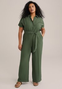 Zeleni kombinezon kratkih rukava s dugmetima sprijeda i vezanjem u struku. Ima široku nogavicu i mekani, teksturirani materijal.