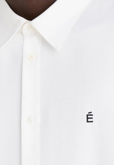 Chemise blanche à boutons avec un col classique et un tissu texturé. Présente un petit logo brodé noir "É" près des boutons.