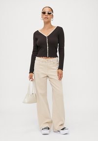 Svart långärmad topp med volangkrage och knäppning, matchad med beige vida jeans och vita sneakers. Accessoarer med en liten vit väska.