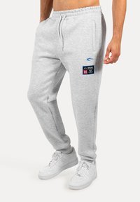 Šedé tepláky vyrobené z bavlněné směsi, s elastickým pasem, bočními kapsami a nášivkou s textem a grafikou na stehně.