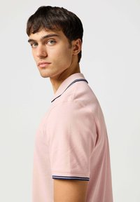Jasnoróżowa koszulka polo z klasycznym kołnierzykiem, z granatowymi akcentami na kołnierzu i mankietach. Wykonana z fakturowanej tkaniny.