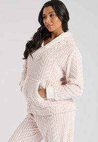 Sudadera con capucha de felpa de punto trenzado en color rosa, con bolsillo frontal y borde de pelaje sintético blanco en el cuello y los puños. Tela suave y texturizada.