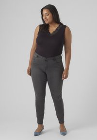 Black sleeveless bodysuit with lace trim, paired with gray skinny jeans. The model wears light blue heels, standing on a plain background.