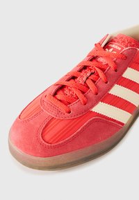 Rød sneakers med overdel i ruskind og tekstil. Har tre hvide striber, snørelukning, struktureret overflade og let farvet gummisål.