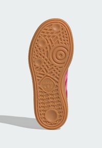 Adidas sko såle i gummigummi med et teksturert mønster som inneholder sirkulære og ovale elementer, samt en logo nær midten. Klare rosa detaljer er synlige.