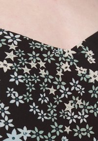 Un tissu noir présente un motif floral avec des fleurs bleu clair et crème ainsi que des étoiles. L'encolure a une forme en V subtile. Texture douce.