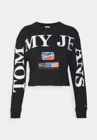 Black cropped long-sleeve t-shirt featuring large white text "TOMMY MY JEANS" and a colorful logo with "New York City Since 1985." Soft cotton material.