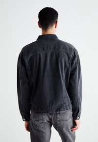 Zwarte spijkerjas met een klassieke kraag, zichtbare stiksels en drukknoopmanchetten. Gecombineerd met grijze jeans die een ontspannen pasvorm laten zien.