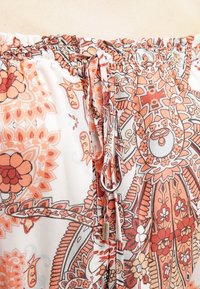 Elastyczny pas z regulowanym sznurkiem na tkaninie z bogatymi w pomarańczowe, czerwone i beżowe, skomplikowane wzory kwiatowe i paisley.