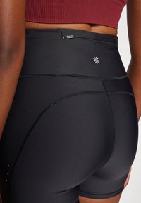 Shorts neri a vita alta realizzati in tessuto liscio e elasticizzato, con cuciture a contrasto, una piccola tasca con zip e un dettaglio con logo.