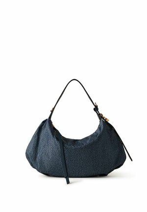 Sac d’épaule texturé bleu foncé en forme de croissant avec une fine bandoulière noire et un pompon en cuir décoratif sur fond blanc.
