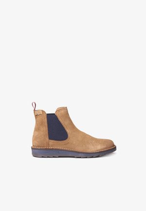 Bottines Chelsea en suède beige avec des panneaux latéraux élastiques bleus, une languette au talon et une semelle en caoutchouc texturé. Design classique de hauteur de cheville.