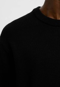 Černý pletený svetr s pleteným kulatým výstřihem. Textura působí jemně a má střední hmotnost, ideální pro vrstvení.