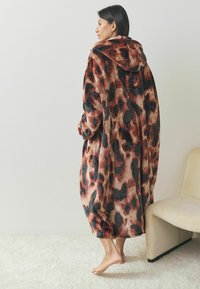 Verkeerd oversized hooded deken in luipaardprint; vervaardigd van zacht, pluche stof in tinten bruin, zwart en beige. Lange mouwen en een ontspannen pasvorm.