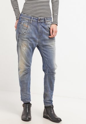 Personne portant un jean bleu délavé à coupe décontractée avec légère usure et des bottines noires, associé à un haut rayé noir et blanc à manches longues.