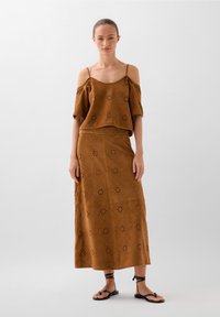Brown perforated fabric two-piece set featuring an off-shoulder top and long skirt, with a loose fit and decorative diamond pattern.
