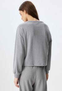 Grijze gebreide pullover met een geribbelde textuur, verlaagde schouders en een cropped ontwerp. De stof lijkt zacht en comfortabel te zijn.