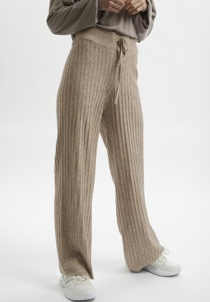 Pantalones de punto acanalado beige con cintura de cordón. Diseño de pierna ancha con rayas verticales. Combinados con zapatillas blancas.