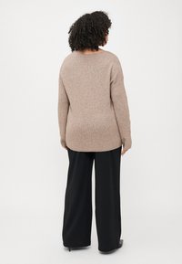 Brown, ribbed knit sweater with a wide neckline and loose fit; paired with black, wide-leg trousers. Smooth texture, casual style.