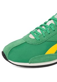 Zielony sneaker wykonany z połączenia gładkiego nylonu i teksturowanego zamszu, z żółtym akcentem i czarną gumową podeszwą. Sznurowadła również są zielone.