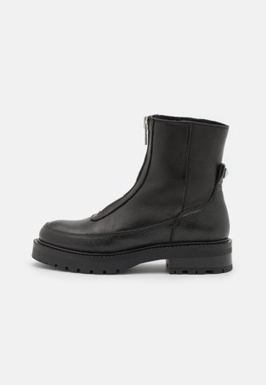 Bottines en cuir noir avec fermeture éclair sur le côté, finition texturée, semelle en caoutchouc et talon épais, présentant des éléments de design minimalistes.