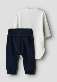 Camisa blanca de mangas largas combinada con pantalones de canalé en un azul marino oscuro, con cintura elástica y puños en los tobillos. Tejido de mezcla de algodón suave.