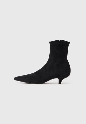 Stivale alla caviglia in suede nero con punta affusolata e tacco kitten. Chiusura con cerniera sul retro, texture liscia e gambo aderente.
