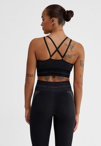 Svart sport-bh med korskorsade axelremmar, ribbad textur och logodetalj. I kombination med svarta högmidjade leggins med nätinslag.
