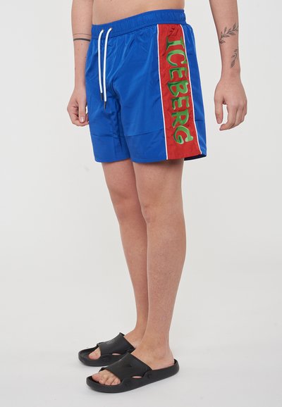 Shorts de bain bleus avec un panneau latéral rouge, portant le mot "ICEBERG" en vert. Fabriqués en matériau léger ; comprennent une taille élastiquée avec cordon.