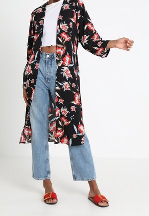 Person wearing blue jeans, white cropped top, black floral long kimono, and red open-toe sandals with gold buckle.