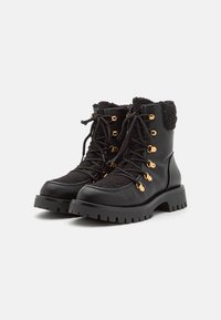 Bottines noires avec un design en matériaux mixtes, comprenant du cuir et un tissu texturé, des œillets dorés, et une semelle épaisse et robuste.