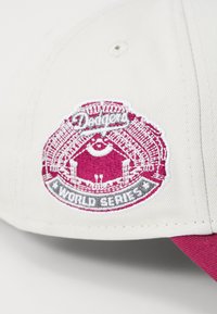 Beige színű baseball sapka bordó hímzett logóval, amelyen a "Dodgers" és a "World Series" felirat található. A sapka struktúrált formájú és sima tapintású.