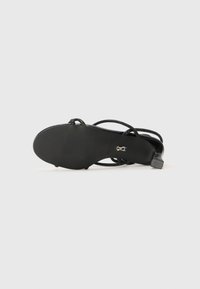 Sandale noire à talons avec des straps tressés ajustables, tige en cuir lisse, talon carré et semelle texturée.