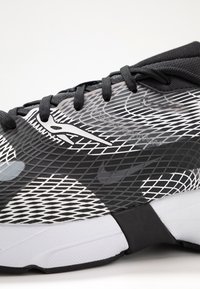 Scarpa sportiva in bianco e nero con tomaia in rete, motivi testurizzati, punta rotonda, lacci piatti e una suola spessa bianca.