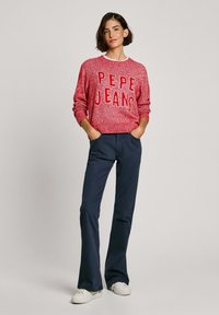 Czerwony sweter z dzianiny z logo "PEPE JEANS", w połączeniu z granatowymi spodniami w stylu dzwonów i białymi trampkami. Prosty kołnierzyk, luźny krój, teksturowany materiał.