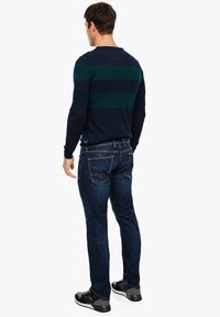 Tmavě modrý svetr se zelenými pruhy, doplněný tmavě modrými džínami. Svetr má kulatý výstřih a dlouhé rukávy. Černé tenisky dokončují vzhled.