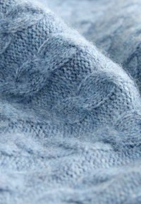 Heledsinine, tekstuurne kudumkangas ribade mustriga. Pehme ja udune pind, mis näitab keerukat õmblust ja erinevat lõngapaksust.