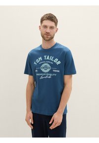 Zila kokvilnas T-kreklu ar "TOM TAILOR" logo gaiši zilā un baltā krāsā. Īsas piedurknes un apaļš kakla izgriezums, gluda tekstūra, brīva piegriezuma.