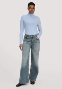 Lichtblauwe coltrui gecombineerd met wijde, vervaagde blauwe jeans. De jeans hebben een vijfzakken ontwerp en zijn gestyled met donkerbruine schoenen.