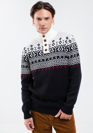 Sweter z dzianiny z wysokim kołnierzem, w kolorze kremowym na górze i ciemnoniebieskiej na dole, z geometrycznymi wzorami w kolorze czarnym i czerwonym, akcentowany brązowymi guzikami.