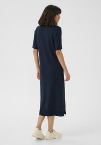 Abito blu navy, lungo fino al ginocchio, realizzato in tessuto morbido con maniche corte e spacco laterale; abbinato a sneakers chiare.