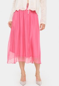 Gonna midi rosa, fluente, realizzata in materiale leggero e trasparente. Presenta una vita arricciata e un orlo liscio. Indossata con tacchi a punta argentati.