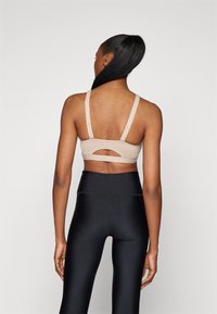 Beige sports-bh med justerbare stropper, utskjæringsdetalj på ryggen, glatt tekstur, kombinert med høy midje svarte leggings.