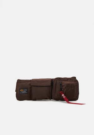 Sac banane marron avec trois compartiments, dont un zippé avec une languette en tissu rouge, présenté sur fond blanc.